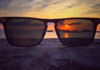 Close-up of sunglasses against sunset sky