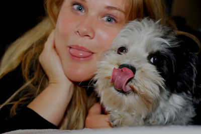 Portrait of young woman and dog sticking out tongue at home