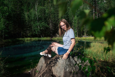 Portrait of woman sitting by lake in forest