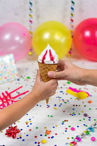 Mom's hand passes the ice cream cone to the child's hand against the backdrop of a colorful decor.