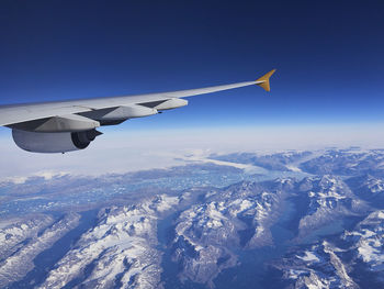 Airplane flying over snowcapped mountains against clear sky