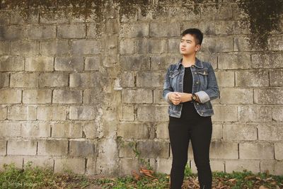 Young woman looking away while standing against wall