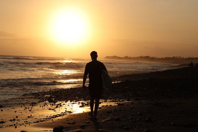 Rear view of man standing on beach during sunset