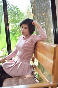 Full length of woman sitting by window against trees