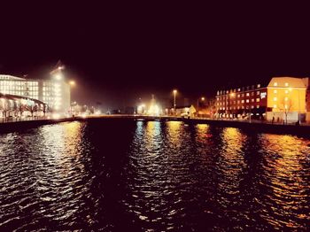 Illuminated city by river against sky at night