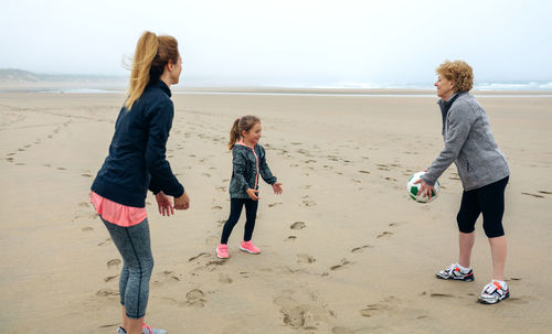 Woman with mother and daughter playing ball at beach against sky