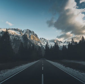 Empty road by trees against sky