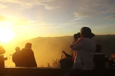 People standing on mountain against sky during sunrise