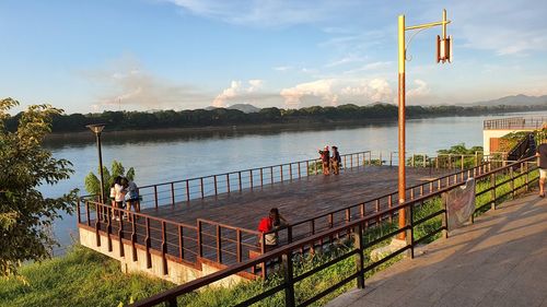 People on railing by river against sky