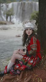 Young asian women wearing miao traditional clothes and hat setting besides the river and waterfall.