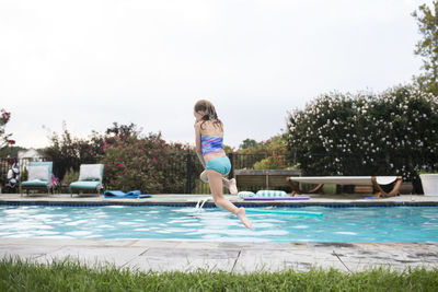 Rear view of blonde girl jumping into backyard swimming pool