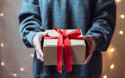 Midsection of woman holding christmas gift against illuminated wall at home