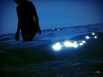 Rear view of silhouette man standing at beach against sky at night