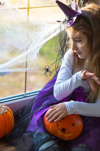 Full length of woman sitting by pumpkin against wall during halloween