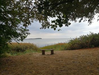 Bench by lake against sky