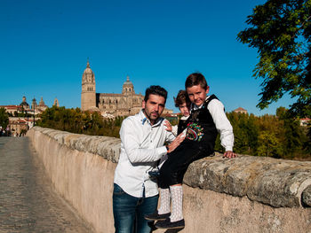 Portrait of man standing children sitting on wall 