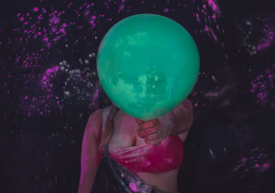 Woman holding balloon while standing in darkroom