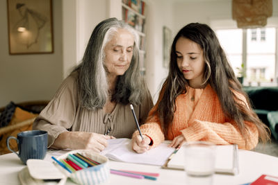 Senior woman assisting granddaughter in homework while sitting at table