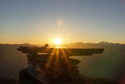 Sun shining over mountain against sky during sunset