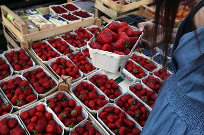 Midsection of woman checking strawberries in crate at market stall