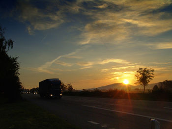 Vehicles on road along landscape at sunset