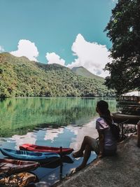 Full length of woman sitting by lake against sky