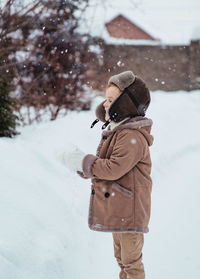 A boy in a winter hat and coat rejoices in the snow. the child catches snowflakes with his tongue. 