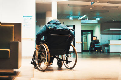 Rear view of man sitting in wheelchair against building in hospital