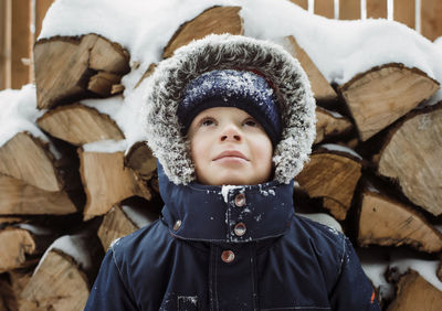 Boy looking up while standing by logs during winter