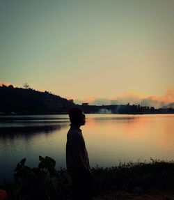 Man standing by lake against sky during sunset