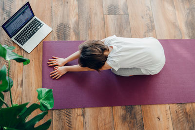 High angle view of girl doing yoga on exercise mat by laptop