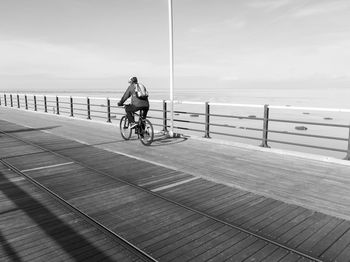 Rear view of person riding bicycle by sea against sky