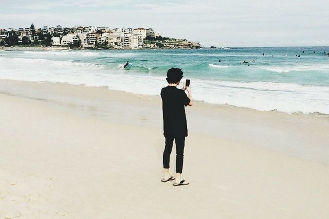 beach, sea, sand, shore, full length, water, lifestyles, leisure activity, rear view, casual clothing, standing, horizon over water, vacations, built structure, building exterior, architecture, walking, sky