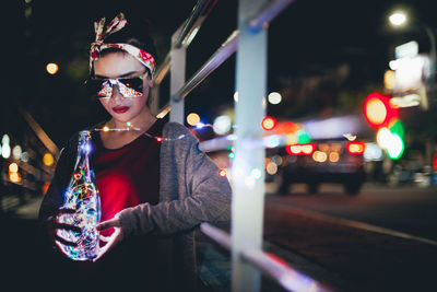 Woman with illuminated lights in bottle standing on street at night