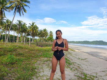 Portrait of smiling young woman standing on beach against sky