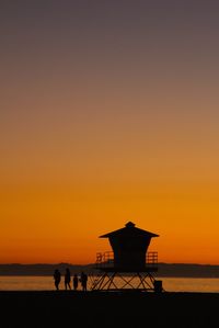 Silhouette lifeguard hut at beach against clear orange sky during sunset