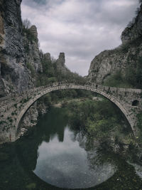 Arch bridge over river against cloudy sky