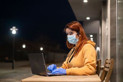 Businesswoman wearing mask using laptop at cafe