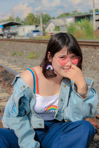 Portrait of smiling young woman wearing sunglasses sitting on railroad track