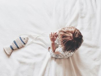 High angle view of baby toddler girl on bed with fish playing 