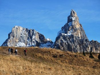 People walking on mountain against blue sky