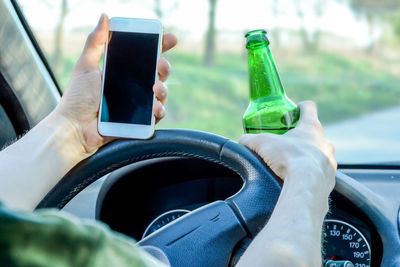 Close-up of man holding mobile phone and beer bottle while driving