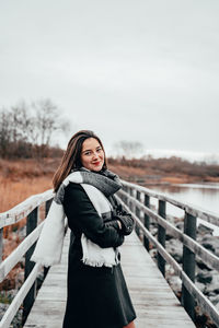 Portrait of young woman standing on footbridge during winter