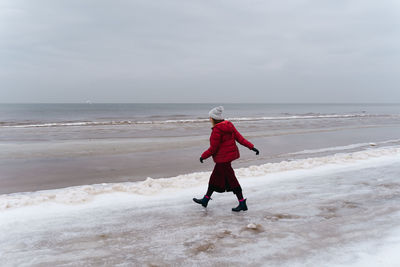 A woman in red walks in winter along the seashore