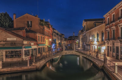 Canal amidst illuminated buildings against sky at night