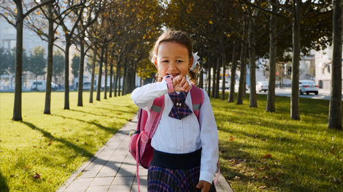 Smiling schoolgirl walking on footpath amidst trees in park