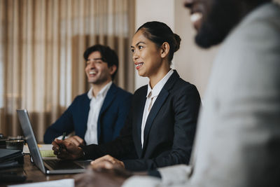 Smiling businesswoman sitting with laptop amidst male colleagues in office