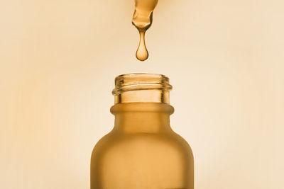 Face serum oil drop with dropper glass bottle pipette on yellow background close up