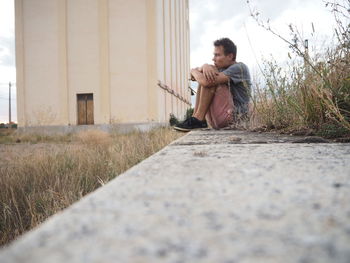 Surface level view of man sitting on retaining wall