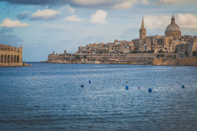 Historic buildings by sea against cloudy sky